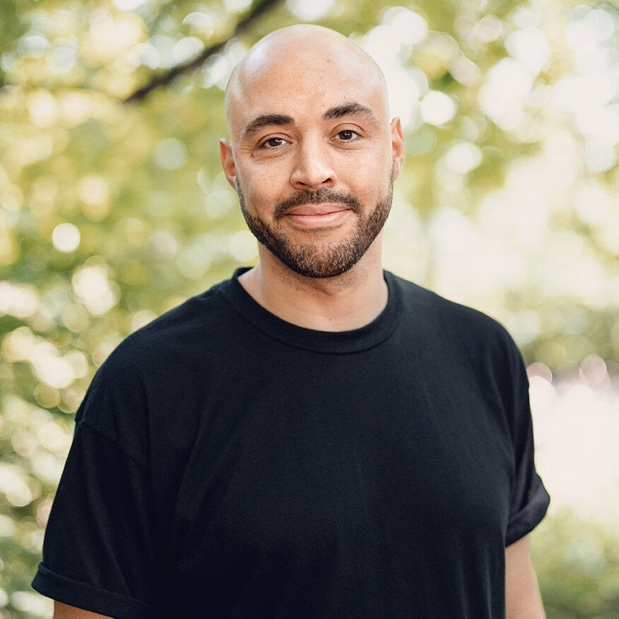 Porträt von Anthony Lynch mit Glatze und Bart, der ein schwarzes T-Shirt trägt, vor einem natürlichen, grünen Hintergrund.