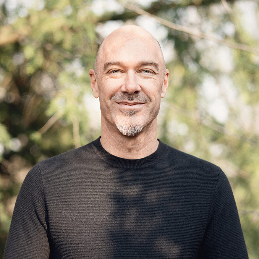 Porträt von Craig Keown, der lächelnd in die Kamera schaut, umgeben von einer natürlichen, grünen Hintergrundszenerie.