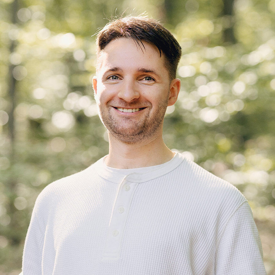 Porträt von Nikolas Wiest, der lächelnd in die Kamera schaut, umgeben von einer natürlichen, grünen Hintergrundszenerie.